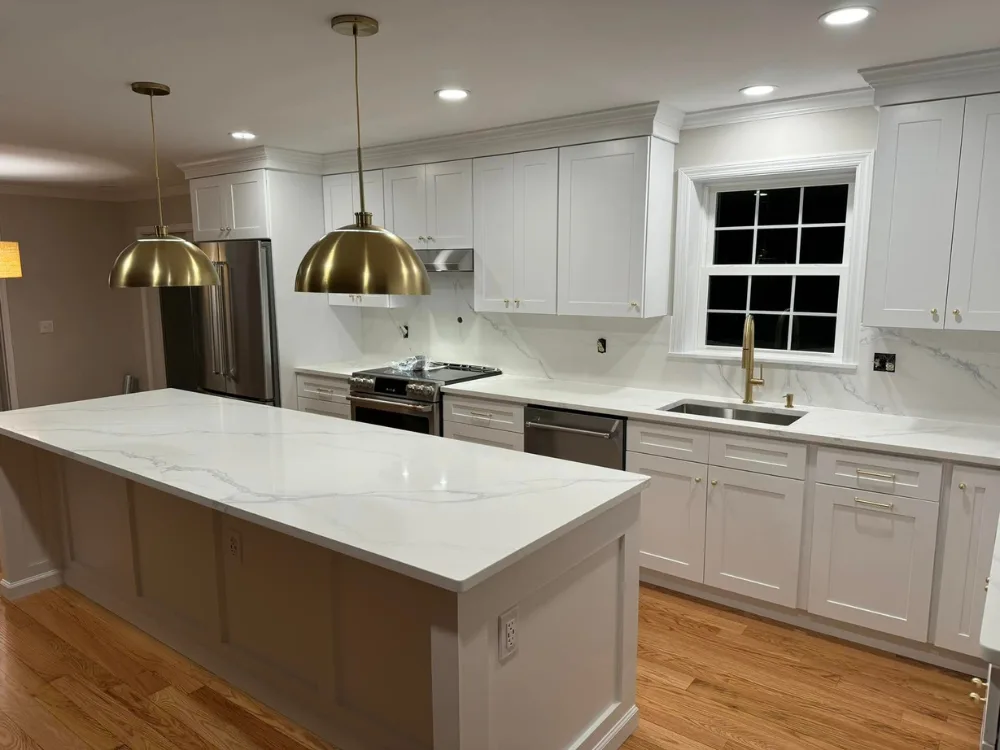 Kitchen remodeling featuring white shaker cabinets, marble countertops, brass fixtures, and hardwood flooring in a modern open layout.