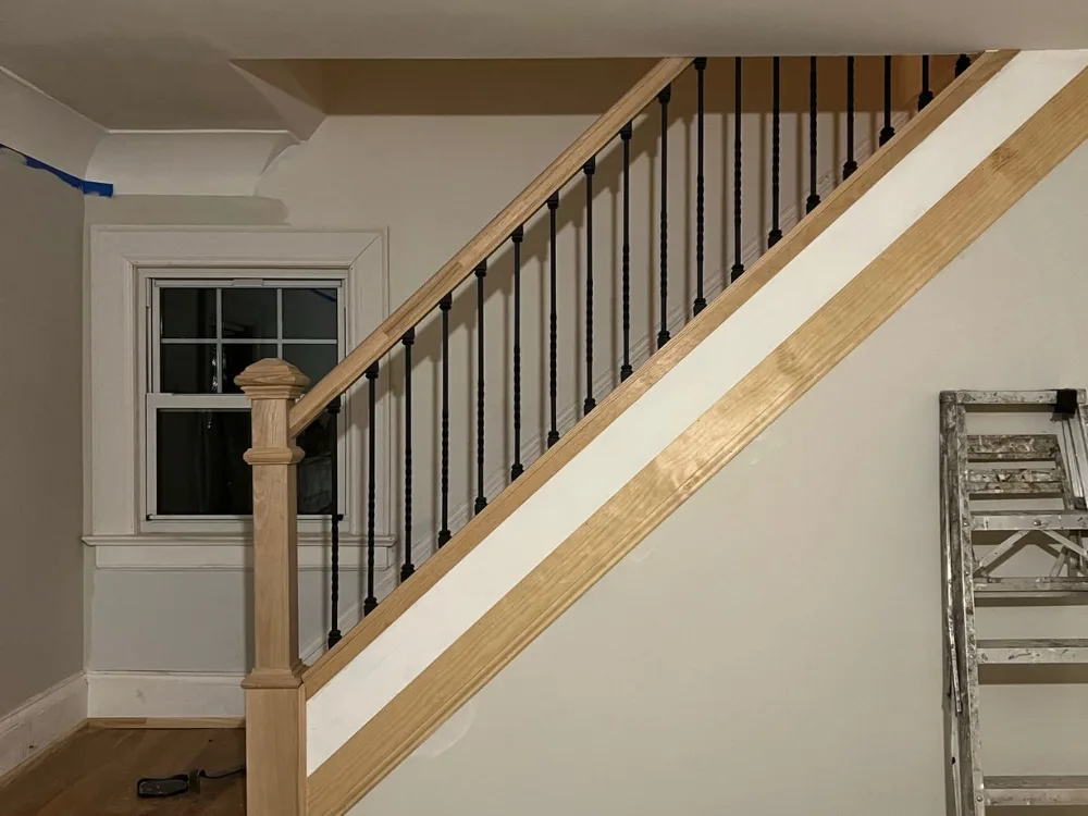 Close-up of Handrail Renovation with a natural wood railing and black metal spindles, along with an unfinished staircase.